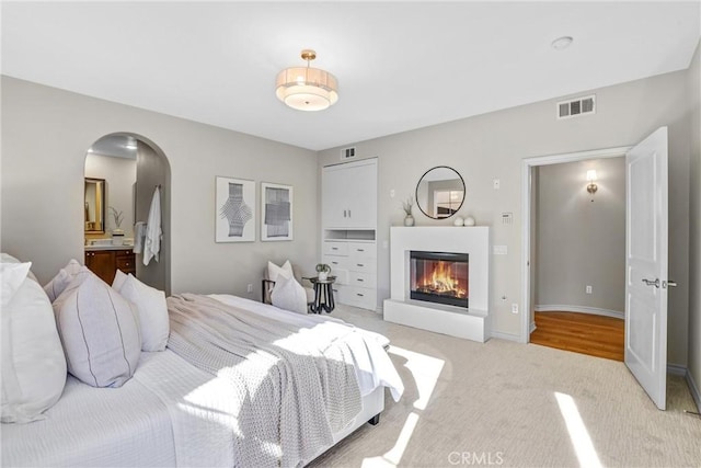 bedroom featuring ensuite bathroom and light colored carpet