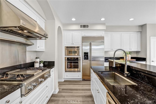 kitchen with sink, wall chimney exhaust hood, white cabinetry, and appliances with stainless steel finishes