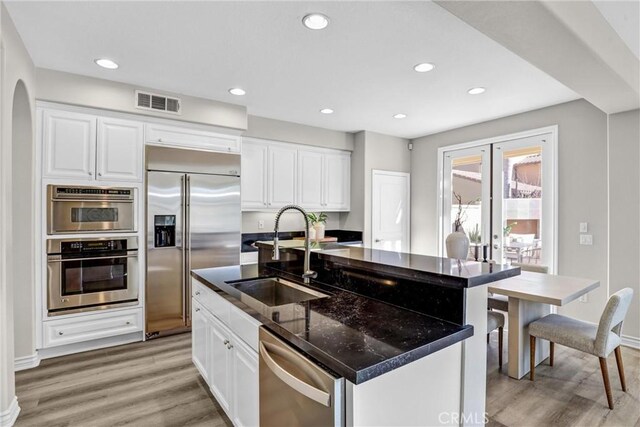 kitchen featuring a center island with sink, white cabinets, dark stone counters, appliances with stainless steel finishes, and sink