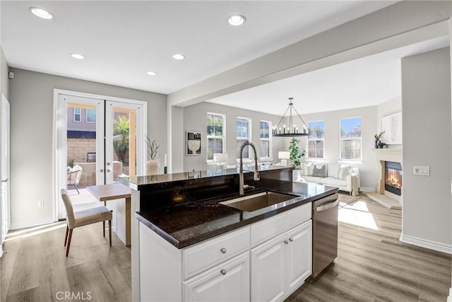 kitchen with sink, white cabinetry, dishwasher, french doors, and an island with sink