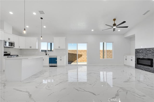 unfurnished living room with ceiling fan, a wealth of natural light, a stone fireplace, and sink