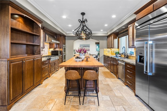 kitchen with exhaust hood, appliances with stainless steel finishes, tasteful backsplash, ornamental molding, and a center island