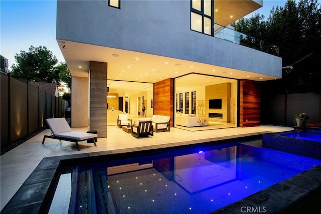 pool at dusk with a patio area and an outdoor living space with a fireplace