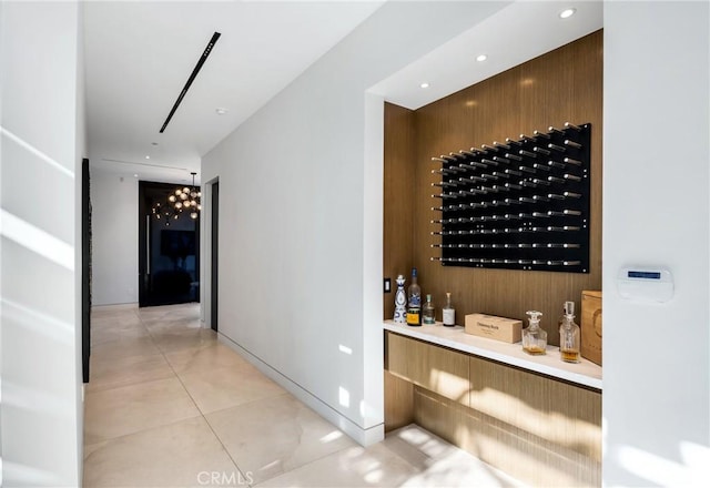 wine area with wood walls, an inviting chandelier, indoor bar, and light tile patterned flooring