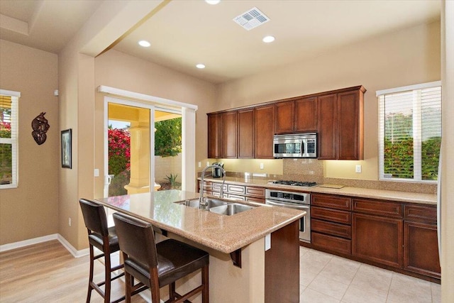 kitchen featuring backsplash, a kitchen bar, sink, a kitchen island with sink, and stainless steel appliances