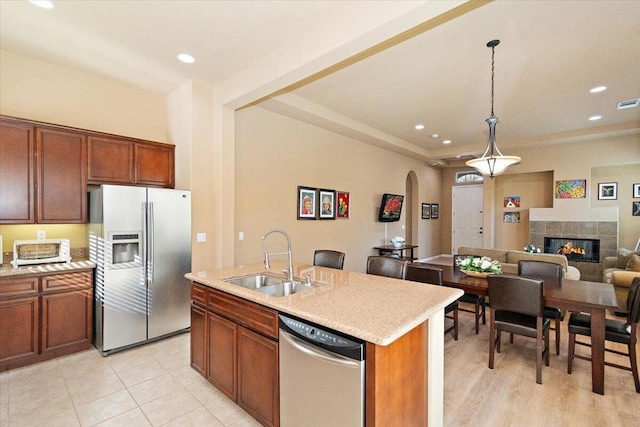 kitchen with appliances with stainless steel finishes, decorative light fixtures, a fireplace, an island with sink, and sink