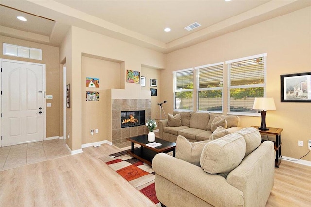 living room with a raised ceiling, light wood-type flooring, and a tile fireplace