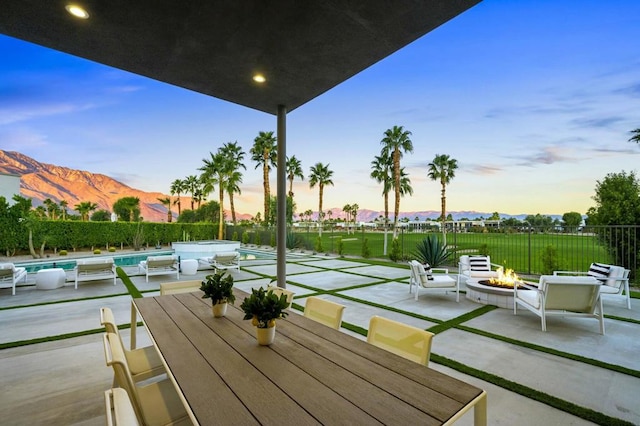 patio terrace at dusk featuring a mountain view, a fire pit, and a fenced in pool