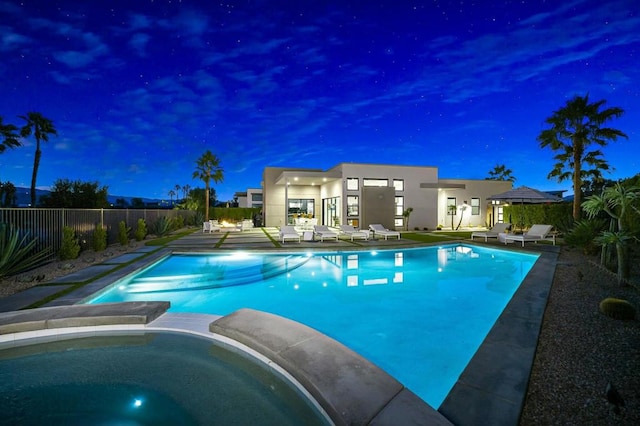 pool at night with an in ground hot tub and a patio area