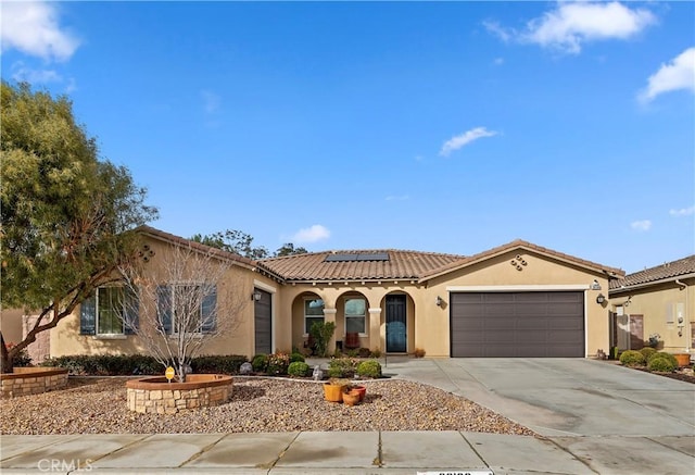 mediterranean / spanish house with a garage, solar panels, a tiled roof, driveway, and stucco siding