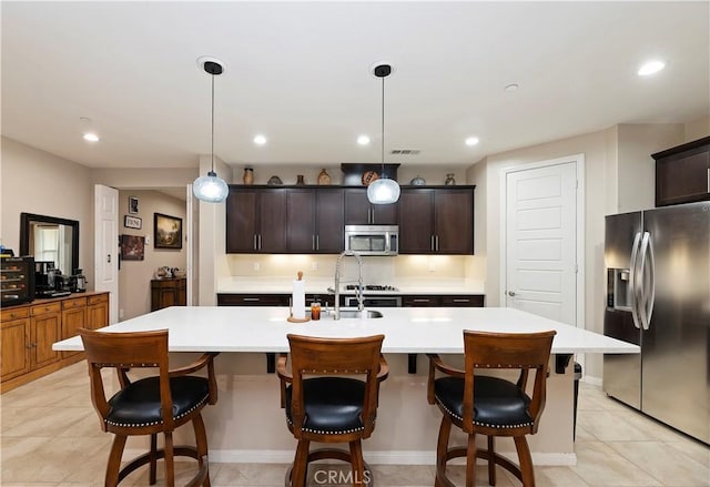 kitchen with a center island with sink, recessed lighting, light countertops, appliances with stainless steel finishes, and a kitchen breakfast bar