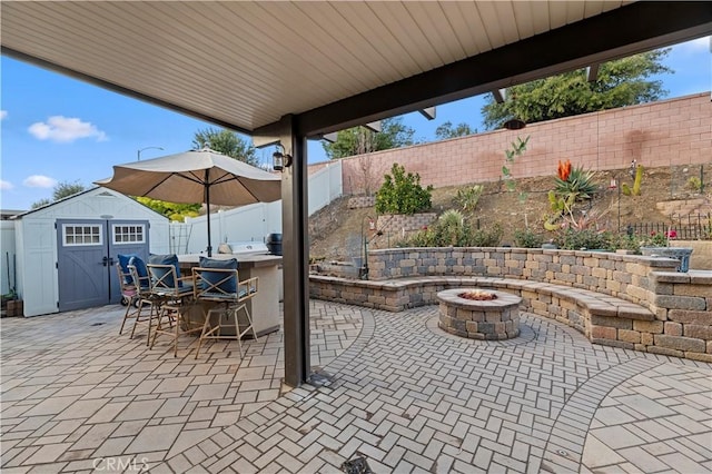 view of patio / terrace with an outbuilding, area for grilling, a shed, a fenced backyard, and a fire pit