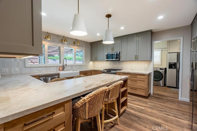 kitchen featuring washer / dryer, sink, appliances with stainless steel finishes, light stone countertops, and decorative backsplash