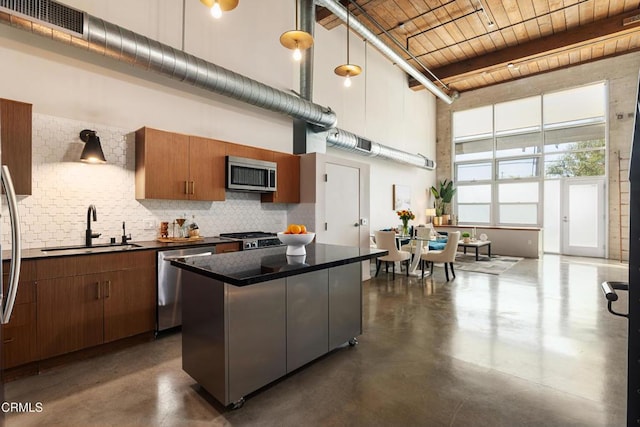 kitchen with a towering ceiling, stainless steel appliances, sink, pendant lighting, and a kitchen island