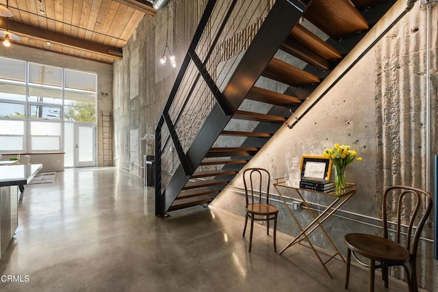 stairway with beamed ceiling, a high ceiling, concrete floors, and wood ceiling