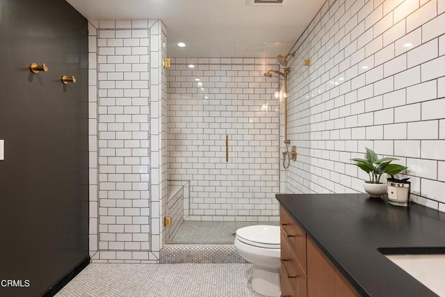 bathroom with tile patterned floors, toilet, vanity, a shower with shower door, and tile walls