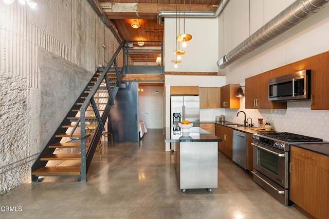 kitchen featuring appliances with stainless steel finishes, a towering ceiling, sink, a kitchen island, and hanging light fixtures