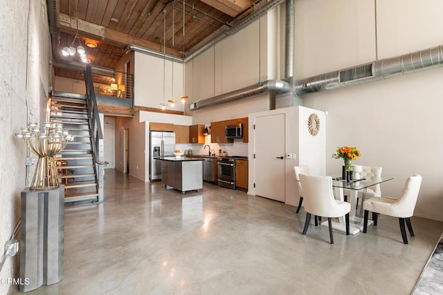 kitchen with appliances with stainless steel finishes, a towering ceiling, tasteful backsplash, pendant lighting, and a kitchen island