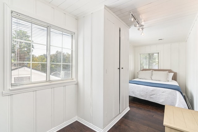 unfurnished bedroom featuring dark wood-type flooring, ornamental molding, multiple windows, and rail lighting