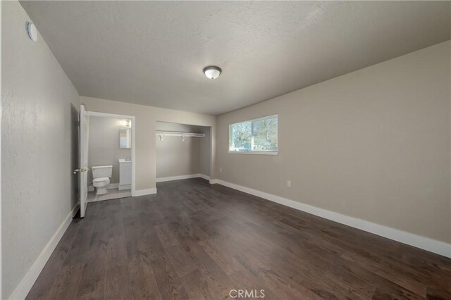 unfurnished bedroom with dark hardwood / wood-style flooring, a textured ceiling, a closet, and ensuite bath