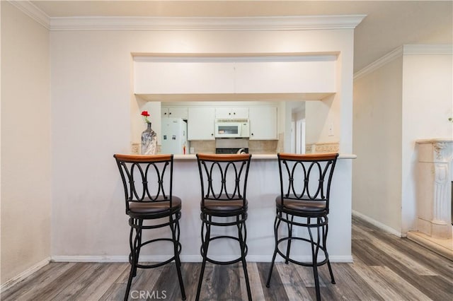 bar with wood-type flooring, backsplash, white appliances, and crown molding