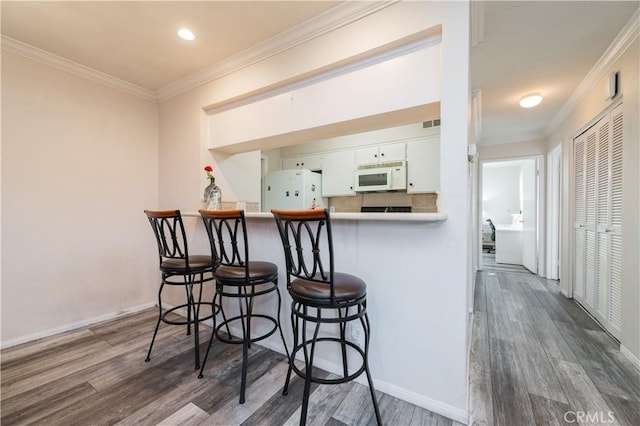 kitchen featuring dark hardwood / wood-style flooring, ornamental molding, white cabinets, and white appliances