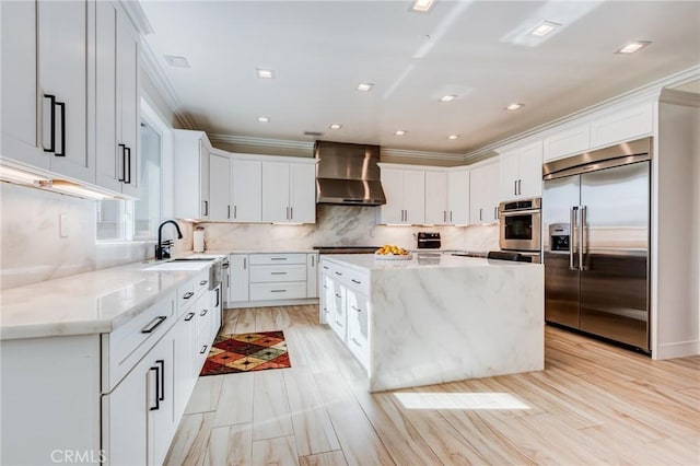 kitchen featuring stainless steel appliances, white cabinets, wall chimney range hood, and a center island