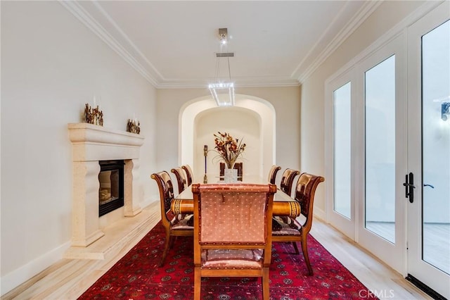 dining area featuring a high end fireplace, french doors, ornamental molding, and light hardwood / wood-style floors