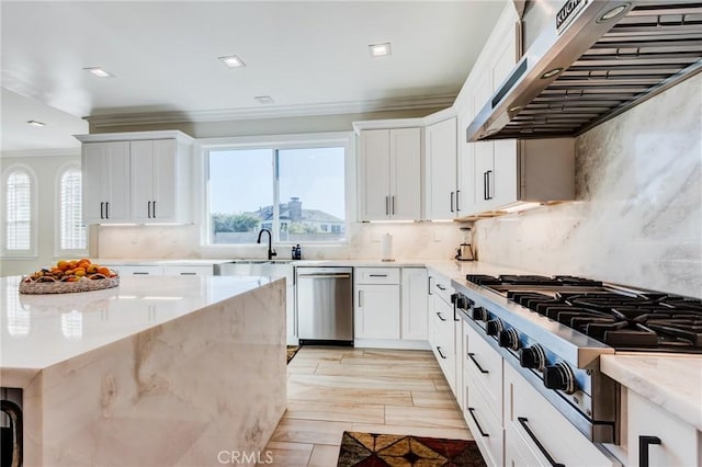 kitchen with white cabinets, decorative backsplash, light stone countertops, wall chimney range hood, and appliances with stainless steel finishes