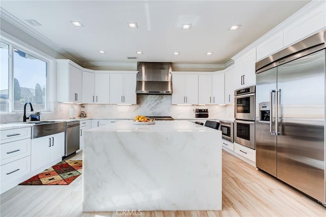 kitchen featuring built in appliances, white cabinets, wall chimney range hood, and a center island