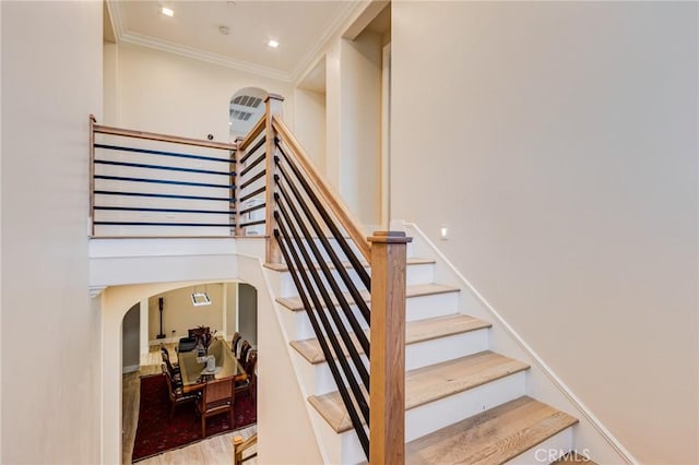 stairway featuring a towering ceiling, ornamental molding, and hardwood / wood-style floors