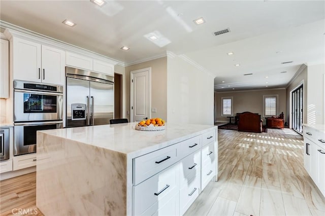 kitchen with built in appliances, white cabinets, light stone countertops, and a center island