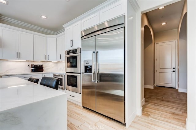 kitchen with built in appliances, light stone counters, tasteful backsplash, light wood-type flooring, and white cabinets