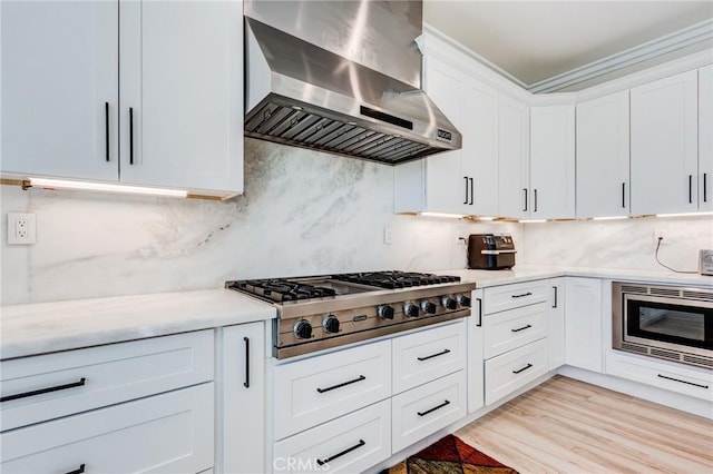 kitchen with wall chimney exhaust hood, decorative backsplash, light wood-type flooring, white cabinetry, and appliances with stainless steel finishes