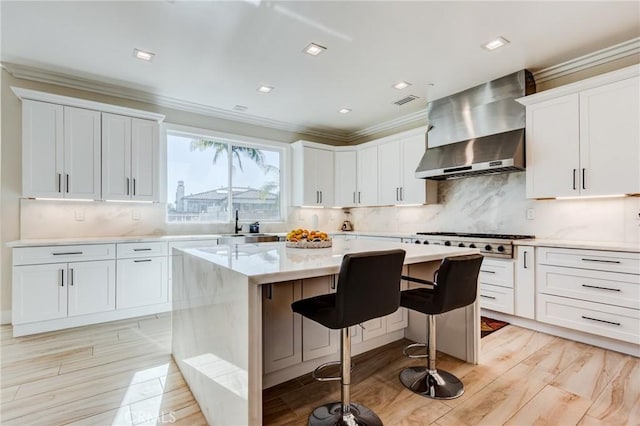 kitchen with white cabinets, a center island, a kitchen bar, stainless steel gas stovetop, and wall chimney range hood