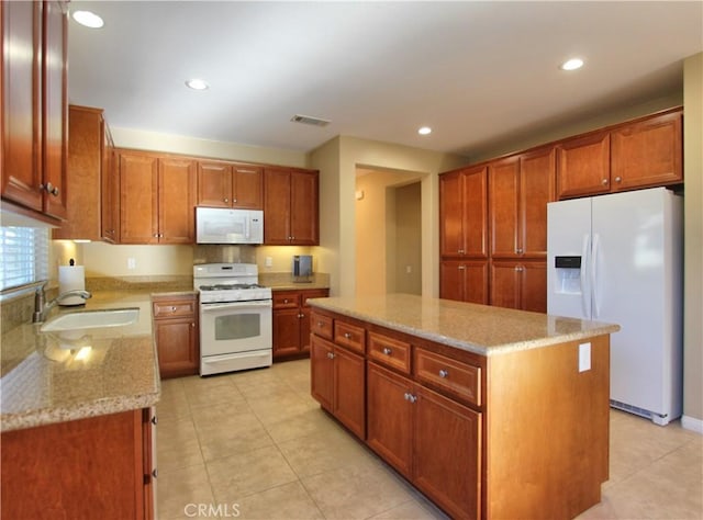 kitchen with white appliances, a kitchen island, sink, light stone counters, and light tile patterned floors