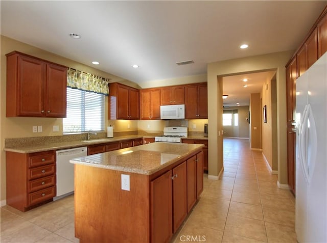 kitchen with white appliances, light tile patterned flooring, a kitchen island, light stone counters, and sink