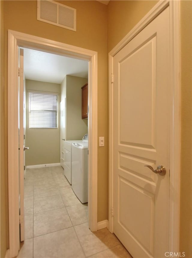 clothes washing area featuring washing machine and dryer, light tile patterned flooring, and cabinets