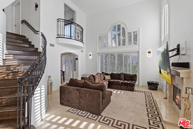 living room with light tile patterned floors, a premium fireplace, crown molding, and a towering ceiling