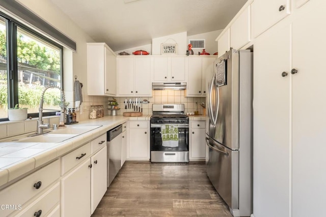 kitchen with white cabinets, appliances with stainless steel finishes, tile counters, and lofted ceiling