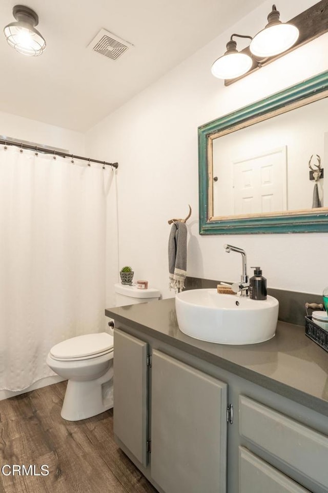 bathroom with a shower with shower curtain, toilet, vanity, wood finished floors, and visible vents