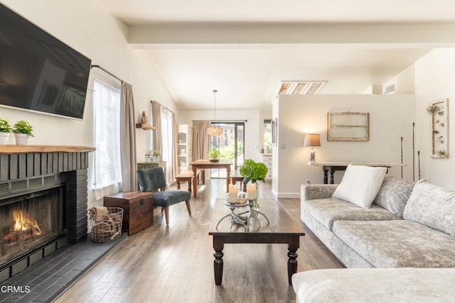 living area featuring vaulted ceiling with beams, a fireplace, wood finished floors, baseboards, and visible vents