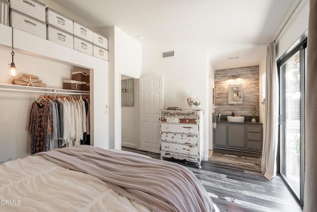 bedroom with wood walls, a sink, visible vents, a closet, and wood finished floors