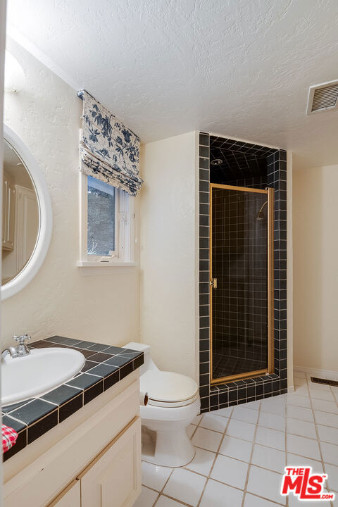 bathroom featuring toilet, tile patterned flooring, walk in shower, a textured ceiling, and vanity