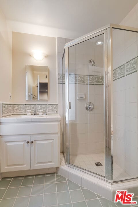 bathroom featuring a shower with shower door, decorative backsplash, tile patterned floors, and vanity