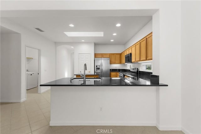 kitchen with a skylight, kitchen peninsula, appliances with stainless steel finishes, light tile patterned flooring, and sink