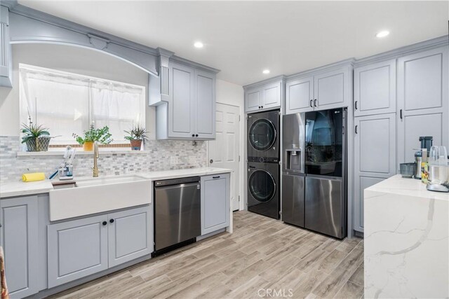 kitchen featuring tasteful backsplash, sink, stacked washer and clothes dryer, gray cabinetry, and stainless steel appliances