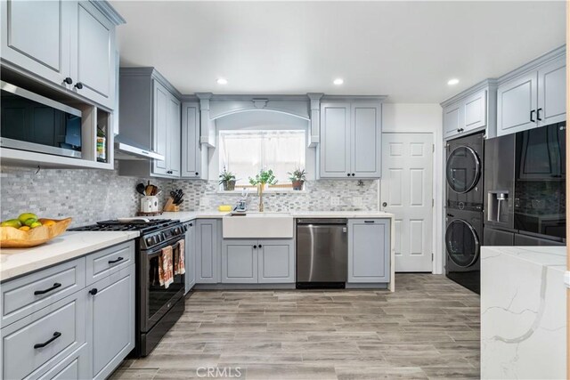 kitchen with tasteful backsplash, sink, appliances with stainless steel finishes, stacked washer and clothes dryer, and gray cabinetry