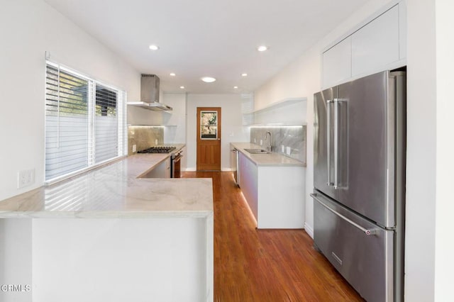 kitchen featuring wall chimney exhaust hood, wood-type flooring, white cabinetry, and stainless steel appliances