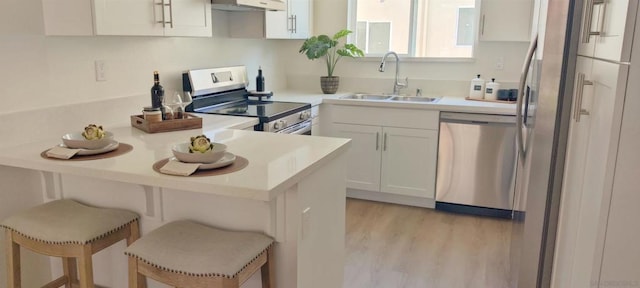 kitchen with a breakfast bar, sink, white cabinetry, light wood-type flooring, and appliances with stainless steel finishes